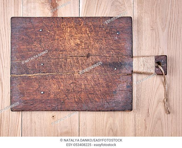 very old brown square cutting board with a handle on a wooden plank background, empty space