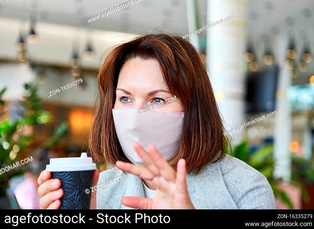 Frau als Gast im Cafe mit Mundschutz wegen Covid-19 Pandemie mit Kaffeebecher