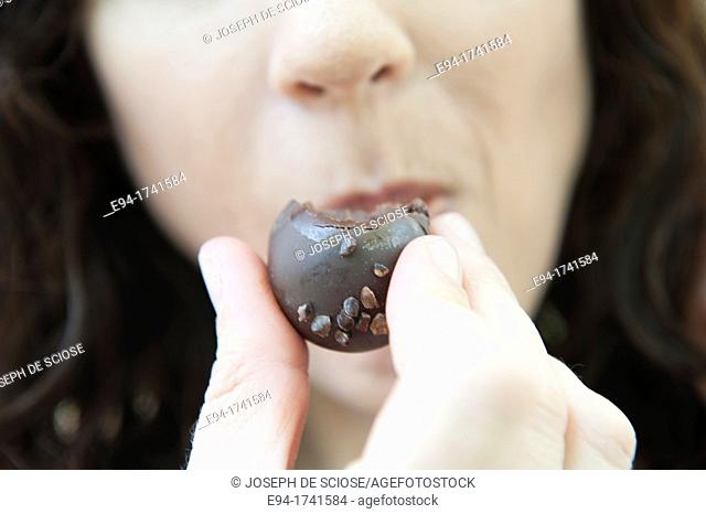 Close up of a woman holding a chocolate truffle in front of her mouth