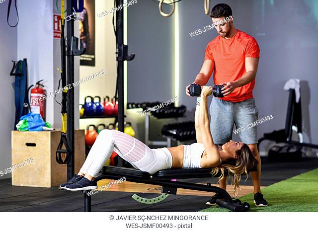 Personal trainer assisting client with weight training, lifting dumbells, lying on bench