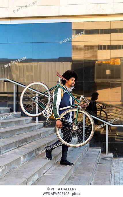 Casual businessman carrying bicycle walking down stairs in the city, Barcelona, Spain