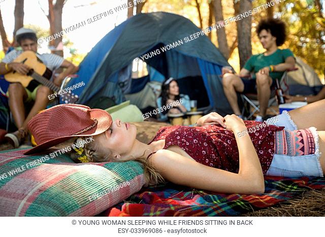Young woman sleeping while friends sitting in background at campsite