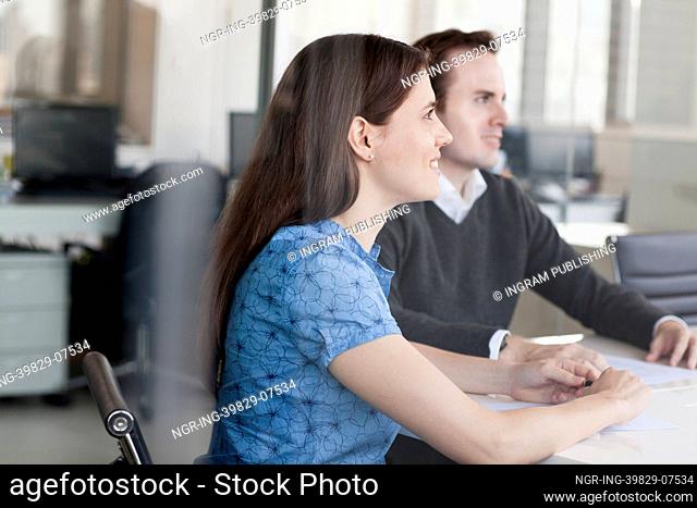 Two business people sitting at a conference table and listening during a business meeting