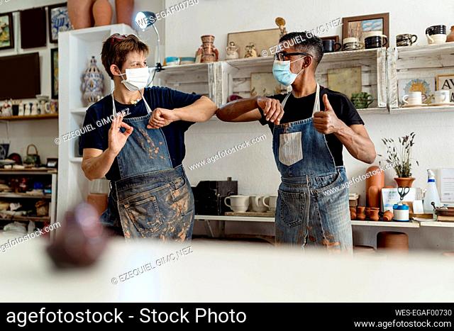Coworkers wearing masks giving elbow bump while standing in workshop
