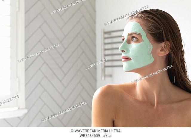 Close-up of thoughtful woman with facial mask looking out of the window in the bathroom