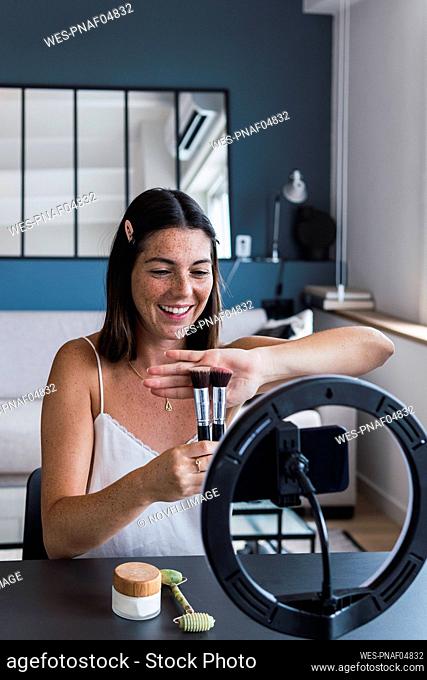 Happy woman showing brushes through smart phone at home
