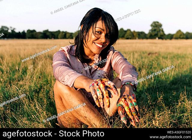 Smiling woman with paint on hands sitting at park during sunny day