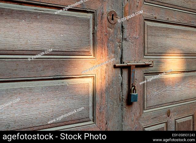 Closeup of rusted metal aged latch and padlock over weathered wooden door