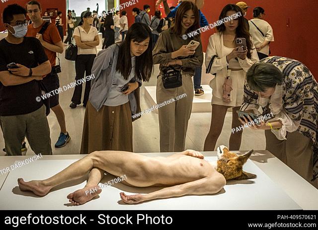 People look at The Doghead a sculpture of naked man with dog head by Sam Jinks during the SUPERNATURAL: Sculptural Visions of the Body exhibition in Taipei