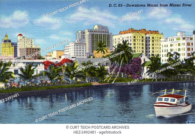 Downtown Miami from the Miami River, Florida, USA, 1941. Vintage linen postcard. There is a boat in the water in the foreground and the city skyline rises in...