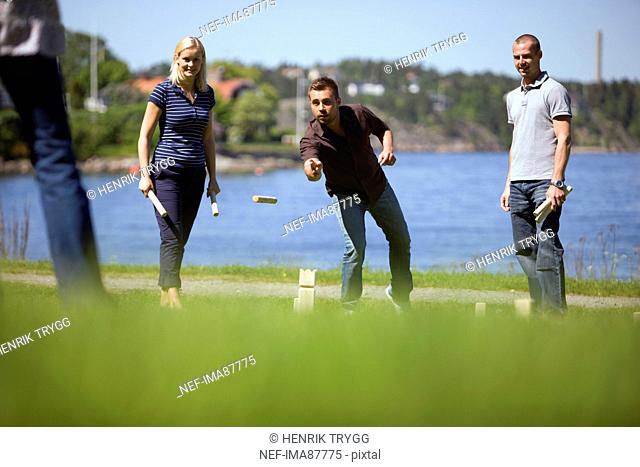 Four adults playing kubb on grass beside sea