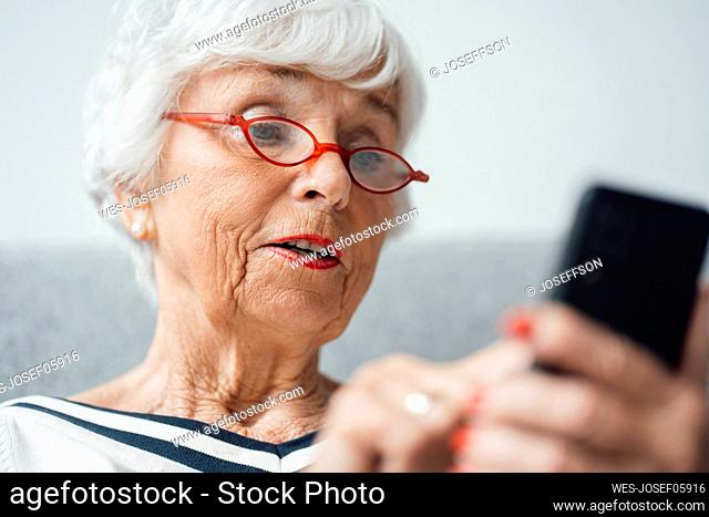 Senior woman wearing eyeglasses using smart phone at home