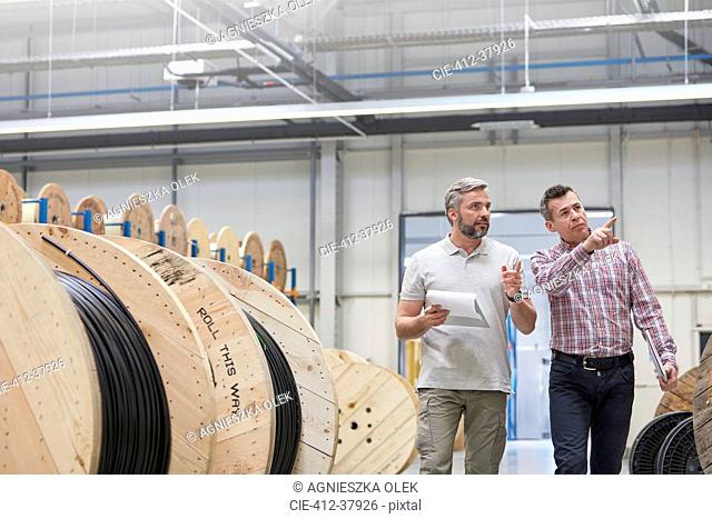 Male supervisor and worker with clipboard walking along spools in fiber optics factory