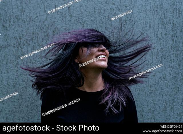 Playful woman tossing hair in front of wall