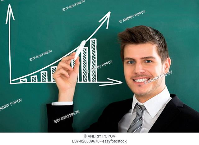 Young Happy Businessman Holding Chalk Front Of Blackboard Showing Graph