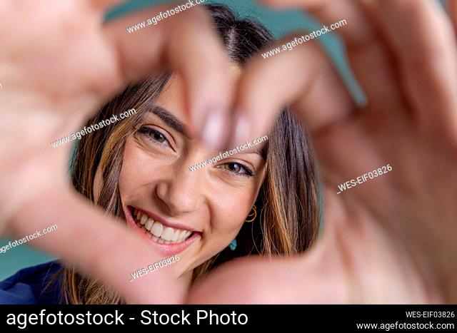 Cheerful young woman making heart shape in front of face