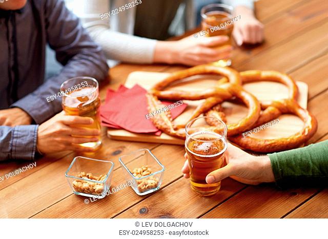 people, leisure and drinks concept - close up of male hands with beer glasses, pretzels and peanuts at bar or pub