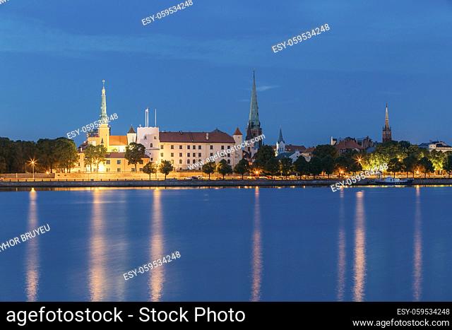 Riga, Latvia. Panoramic Picturesque Urban View Of Daugava Or Western Dvina River In Central Part Of City With Famous Landmarks In Bright Illumination Under Blue...