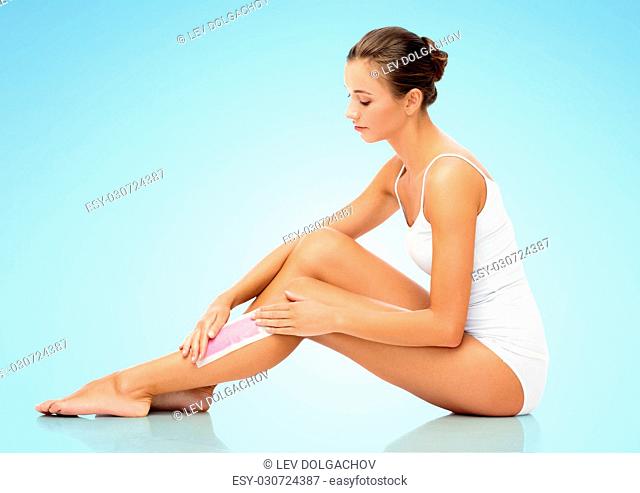 beauty, hair removal and people concept - beautiful woman applying depilatory wax strip to her leg skin over blue background