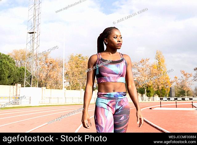 Confident young sportswoman looking away while standing on track during sunny day