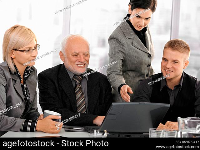 Businesspeople at meeting in office looking at laptop computer, businesswoman pointing at screen, smiling