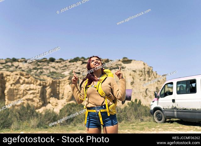 Smiling woman wearing backpack pointing on sunny day