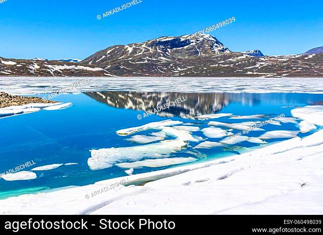 Frozen turquoise lake Vavatn panorama in summer landscape and mountains with snow in Hemsedal Norway
