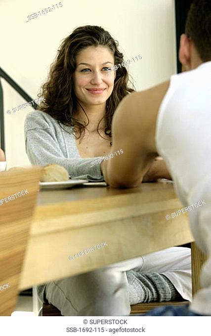 Young woman sitting at a dining table across from a young man