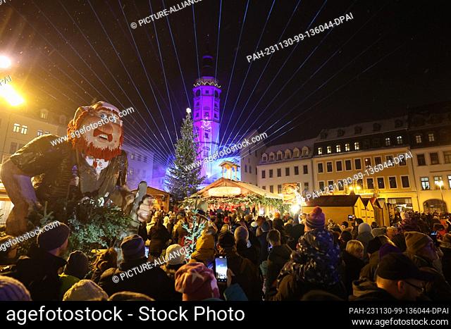 30 November 2023, Thuringia, Gera: Visitors stand at the opening of the Christmas market, at the fairytale market and watch a laser show depicting the fairytale...