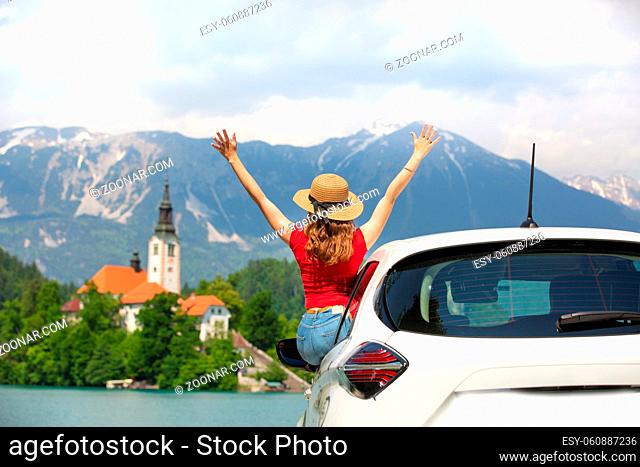 Summer vacation car road trip freedom concept. Happy woman cheering joyfuly by rising hands to the sky enjoying beautiful view of lake Bled, Slovenia, Europe