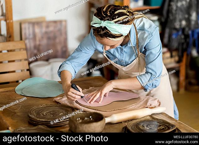 Potter with hand tool working at art studio