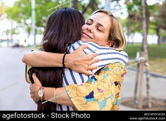 Smiling woman with eyes closed hugging female friend at park