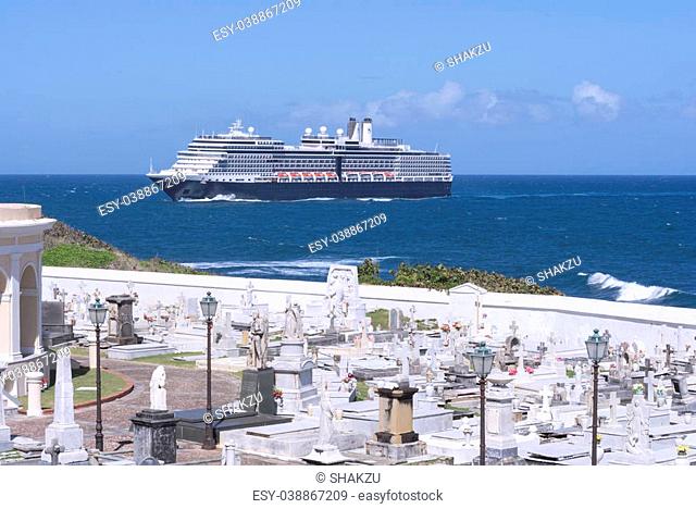 Santa Maria Magdalena de Pazzis cemetery on edge of ocean as huge passenger cruise ship goes towards port in San Juan, Puerto Rico under a blue sunny sky