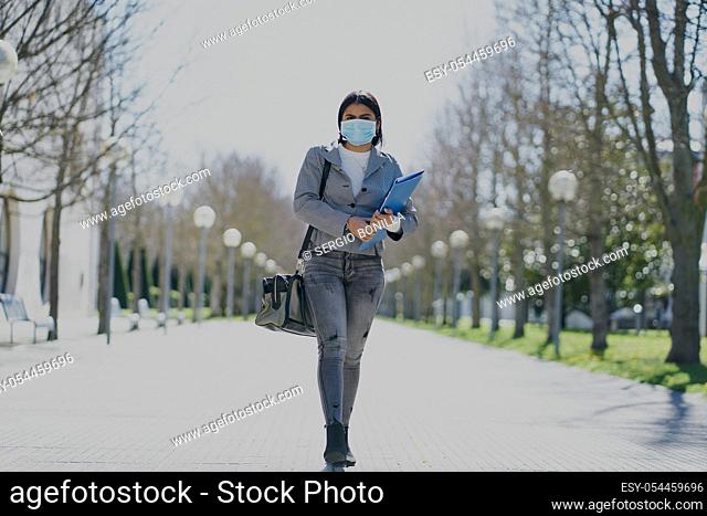Girl putting on a protective mask to avoid contagion while walking down the street. Coronavirus concept