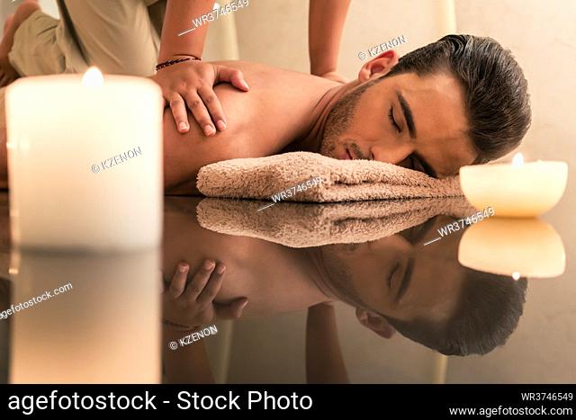 Young muscular man enjoying the healing benefits of traditional Thai massage at luxury spa and wellness center