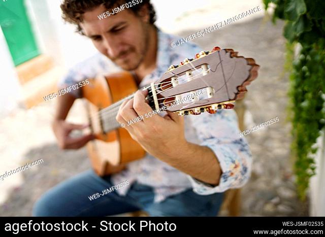 Musician playing Flamenco guitar sitting on chair