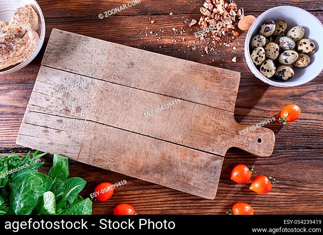 Fresh herbs, nuts, tomatoes and boiled meat on a wooden table with a kitchen board and copy space. Healthy salad products. Flat lay