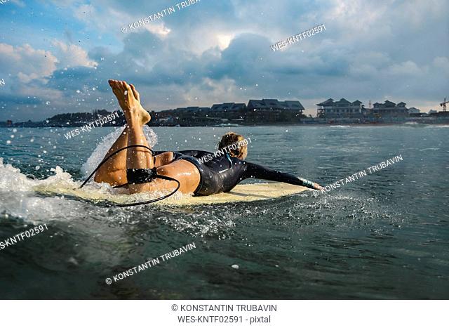 Indonesia, Bali, Canggu, female surfer lying on surfboard