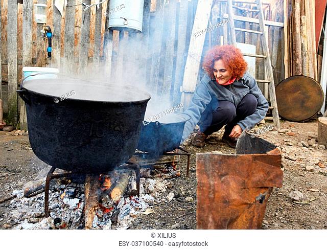 Curly haired peasant woman boiling water in very big cast iron pots