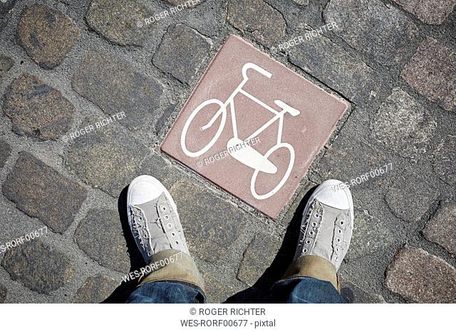 Person standing next to pictogram with bicycle on cobblestone pavement