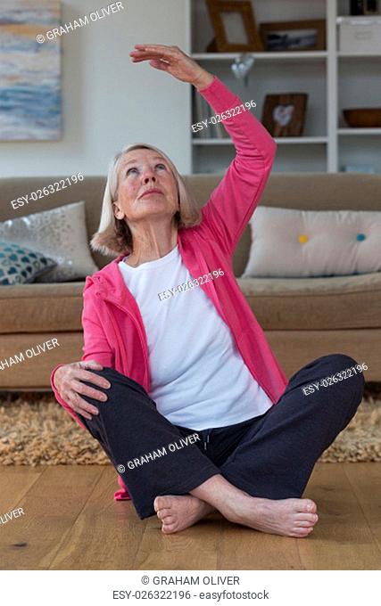 Senior lady stretching in her home. She is sitting on the floor in her living room