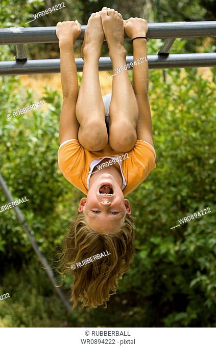 Girl hanging upside down from a jungle gym