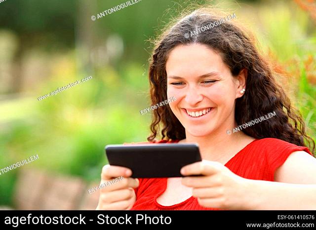 Happy woman in a park watching videos on horizontal smart phone in a park