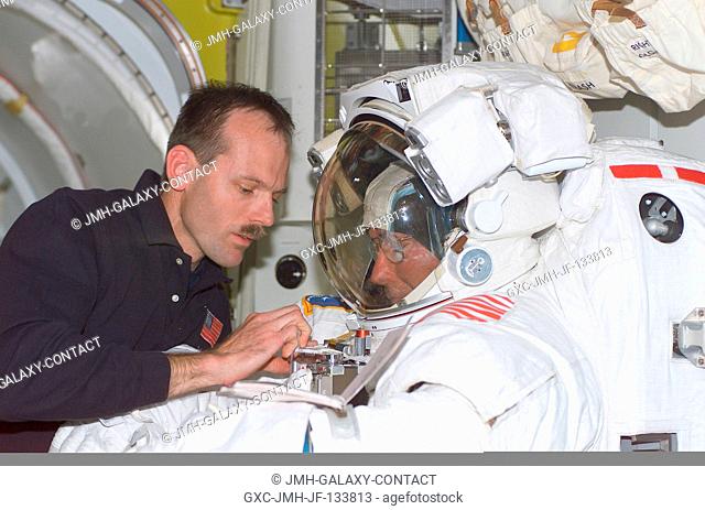 In the shirt sleeve environment of the International Space Station (ISS), astronaut Steven L. Smith (left) assists astronaut Jerry L