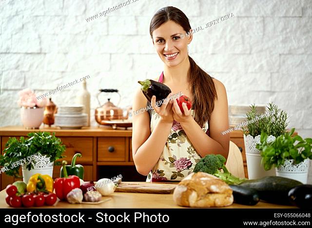 beautiful young woman, brunette holds aubergine and tomato in the kitchen at a table full of organic vegetables