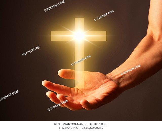 Male hand with a shining cross, religion concept image