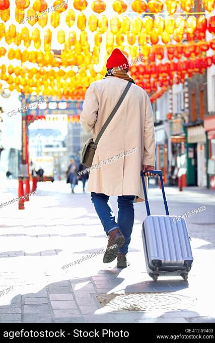 Male tourist pulling suitcase on sidewalk in Chinatown, London, UK