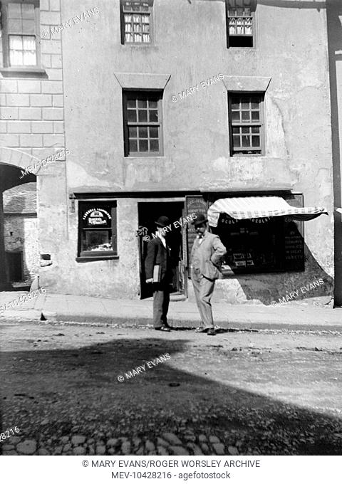 Two men standing outside a confectionery and tobacco shop in the High Street, Haverfordwest, Pembrokeshire, Dyfed, South Wales look straight at the camera