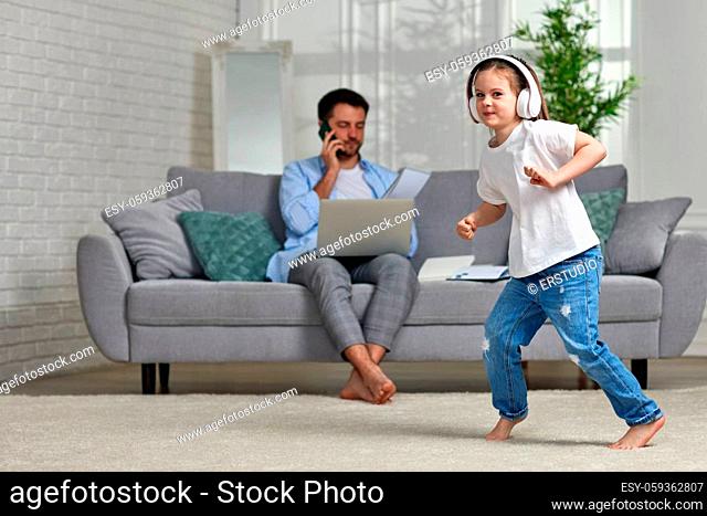 Cheerful playful kid dancing and unhappy busy dad working with laptop at home