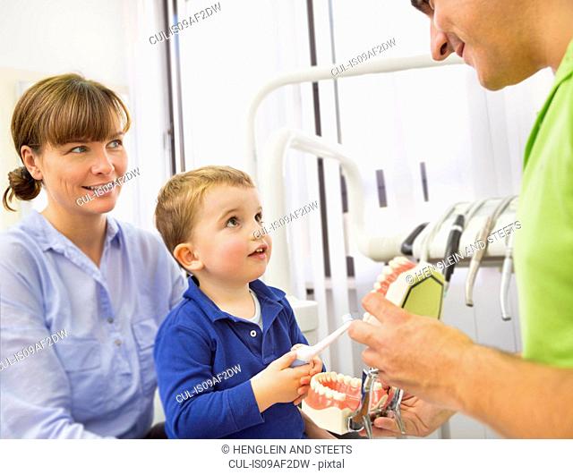 Dentist teaching boy on mothers lap how to brush teeth